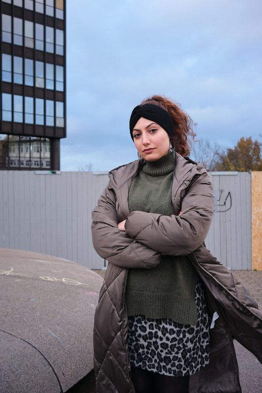 Portrait von Sima vor einem stillgelegtem Springbrunnen vor dem Rathaus Essen. Aufgenommen am 25.11..2022 in Essen.

Sima ist 32 Jahre alt und 
kommt aus Sanandaj in 
Kurdistan, im Westen Irans.
Vor fünf Jahren kam sie nach Deutschland um in Dortmund Soziale Arbeit zu studieren, nachdem sie im Iran einen Bachelorabschluss in Wirtschaftsingenieurwesen gemacht hatte.
Schon als Teenager  schrieb sie in ihr Tagebuch: "Warum werden die Jungs anders als die Mädchen behandelt? Warum haben die Jungs Freiheiten, die ich nicht habe?"  Sie störte sich an diesen patriarchalischen Strukturen, das Männer über sie bestimmen sollen, war eine Horrorvorstellung für sie. 
Später organisierte sie eine Frauenrechtsdemonstration an ihrer Universität und wurde daraufhin vom Geheimdienst verhört und bedroht, was sie nicht davon abgehalten hat, 
sich im Verborgenen weiter 
zu engagieren. 

Zitat:"Oft denke ich: Wenn ich mutiger wäre, wäre ich jetzt im Iran. Lange hatte ich ein schlechtes Gewissen hier in Deutschland in Sicherheit zu sein, während in meinem Heimatland Menschen sterben. Diese psychische Belastung ging so weit, dass sogar mein Studium und meine Arbeit darunter litten. Es war so als wollte ich mir irgendwie selbst das Leid zufügen, was meine Landsleute im Iran gerade erleiden. Es hat eine Weile gedauert, bis ich verstanden habe, dass das nicht der richtige Weg ist. Ich denke, im Moment ist es die Aufgabe jeder Iraner:in in der Diaspora sich hier in Deutschland so gut wie möglich für die Revolution zu engagieren."
